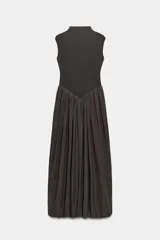 Vestido largo sin mangas con cuello subido, confeccionado con una parte superior ajustada y una falda amplia de tul plisado a tono. Cuenta con cierre de cremallera oculta en la espalda.