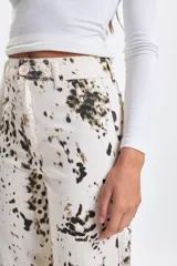 Pantalon de jean de corte ancho y tiro medio, color crudo con estampado de manchas irregulares en tonos oscuros. Presenta un diseño de pierna recta y ruedo desflecado.