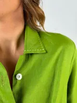 Vestido camisero largo color verde lima, con cuello camisero, mangas largas con puños abotonados, cierre frontal con botones y lazo anudado en la cintura.