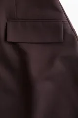 Vestido corto de sarga color marrón oscuro, con escote redondo, manga larga y cintura entallada con pinzas. Presenta bolsillos ribeteados con solapa en la parte delantera.