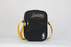 Morral cruzado de nylon negro con textura de rombos, con el logo de Los Angeles Lakers en tonos morado y dorado, y el logo de la NBA en blanco en la parte inferior. Posee correa regulable de color amarillo.