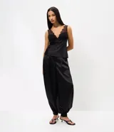 Pantalón aladín negro de satén, con diseño de caída amplia, cintura ajustada y botamanga con puño elástico.