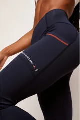 Calza deportiva de tiro alto color negro, confeccionada en poliamida de alta performance. Presenta bolsillos laterales con costuras en color verde neón y detalle de estampado reflectante en la pierna izquierda.
