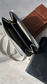 Cartera portacelular con correa larga, cierre con cremallera y solapa con broche imantado.