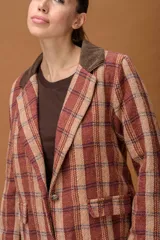 Blazer de tejido con diseño a cuadros en tonos tierra, con solapa de pana en color marrón oscuro, cierre frontal con botón y bolsillos laterales con solapa.
