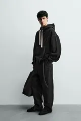 Sudadera tipo hoodie de corte relajado, color negro, con interior perchado. Presenta capucha ajustable con cordones en color crudo, bolsillo frontal tipo canguro y costuras a contraste en color blanco. Posee puños y ruedo en rib.