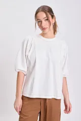 Remera color crudo con cuello redondo, mangas cortas abullonadas y pespuntes decorativos en color marrón claro.
