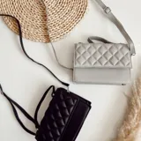 Cartera bandolera negra de ecocuero con diseño acolchado en rombos. Tiene asa corta superior y correa larga desmontable y regulable.