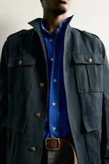 Chaqueta estilo militar relaxed fit de color azul marino, confeccionada en mezcla de algodón y lino. Presenta cuello subido, manga larga con puño abotonado, hombros con trabillas y cuatro bolsillos delanteros de parche con solapa. Se cierra al frente con botonadura metálica dorada.