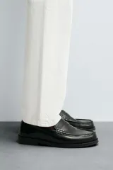Mocasín de vestir tipo penny loafer, fabricado en piel con acabado brillante, horma redonda y suela con ligero tacón.