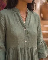 Vestido corto verde militar de lino, con cuello mao, escote en V con botones, mangas tres cuartos acampanadas con volados y falda con volado en el ruedo.