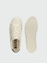 Zapatillas Boss modelo Aiden Tenn Grained, color blanco marfil con detalles en negro en el talón y líneas laterales, con la inscripción de la marca en el lateral.
