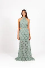 Vestido largo de encaje con patrón circular, color lila, de corte halter con tiras cruzadas al cuello y aberturas laterales en la cintura.