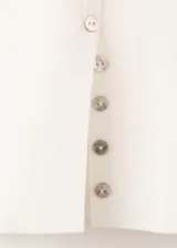 Chaleco de punto fino y diseño entallado, color marfil, con cuello redondo, manga corta y cierre frontal con pequeños botones.