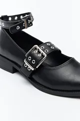 Zueco de diseño contemporáneo con inspiración punk, confeccionado en material símil cuero, con doble tira con hebillas metálicas y tachas, y taco bajo.