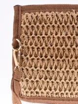 Monedero tipo sobre de paja trenzada color arena, con borde y correa de mano marrón.