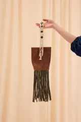 Bolso estilo bucket de cuero marrón, con flecos largos de gamuza verde oliva en la base y asa de mano tejida en macramé color natural.