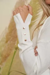 Buzo tejido de punto color blanco, con escote en V, mangas largas con detalle de botones en los puños y aberturas laterales en el ruedo.