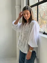 Camisa blanca de corte holgado y manga larga, con delicados bordados florales en tono gris claro en el frente.