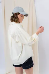 Camisa verde pastel de algodón, corte oversize, con cuello camisero, cierre con botones, mangas largas con puños con volados de encaje blanco, dos bolsillos frontales con solapa y ruedo irregular. 