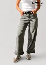 Pantalón de jean estilo palazzo, color gris claro, con corte amplio y fluido. Presenta un dobladillo ancho fijo en la botamanga, cierre frontal con botón y cremallera, y trabillas para cinturón. Incluye un cinturón negro con hebilla metálica.