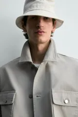 Cazadora de corte relajado confeccionada en tejido de algodón compacto con efecto lavado. Presenta cuello de solapa, manga larga con puños abotonados y cierre frontal de botones. Incluye cuatro bolsillos frontales: dos de plastrón con solapa en el pecho y dos bolsillos dobles de plastrón en la cadera.