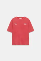 Remera de corte oversize con efecto lavado, color rojo, cuello redondo y manga corta con hombro caído. Presenta un estampado pequeño en el pecho con el logo de la marca y un dibujo lineal de una taza de café.