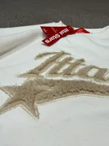 Buzo de cuello redondo color blanco off-white, con diseño de estampa frontal bordada en relieve con la palabra Ittai y una estrella.