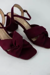 Sandalia de tacón cuadrado medio, confeccionada en material textil tipo gamuza color negro. Presenta un diseño de tiras cruzadas con nudo en la parte delantera y una tira ajustable con hebilla metálica en el tobillo.