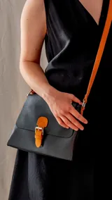 Bandolera negra de cuero sintético con correa larga naranja y cierre con hebilla naranja.