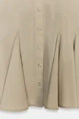 Vestido corto tipo camisero color beige, con cuello solapa, manga corta y cierre frontal con botones a presión. Presenta un diseño con pliegues en el bajo que le otorgan volumen.