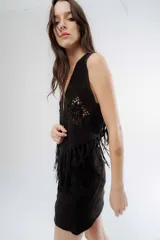 Chaleco negro de estilo boho, confeccionado en semigamuza con detalles de tejido de punto en el frente y la espalda. Presenta un diseño sin mangas con flecos en el ruedo, aportando movimiento y textura a la prenda.