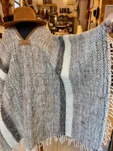 Poncho de lana virgen tejido en telar con diseño de rayas y detalles de cuero en el cuello, con terminación de flecos en los bordes.