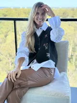 Chaleco negro con cierre frontal de botones, decorado con flores bordadas a mano y costuras decorativas en los bordes.