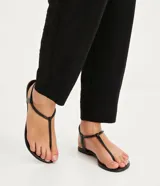 Sandalia plana de mujer color dorado metalizado, con diseño minimalista de tira fina que une la puntera y el empeine, y tira elástica fina alrededor del tobillo.