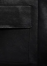 Chaqueta corta de efecto piel en color negro, con cuello de solapa, cierre frontal de botones y dos bolsillos de parche con solapa en la parte delantera. Presenta un diseño recto y forro interior.