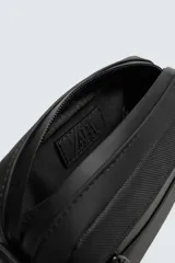 Bandolera negra con acabado engomado y textura. Cuenta con un compartimento principal con cierre de cremallera, un bolsillo plano interior y un asa de hombro ajustable y extraíble.