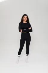 Conjunto deportivo de tres piezas en color negro, compuesto por un top de manga larga con cuello redondo y logo estampado, un top de bretel ancho y una calza chupín de tiro alto. El diseño presenta detalles de tejido con textura en zonas estratégicas.