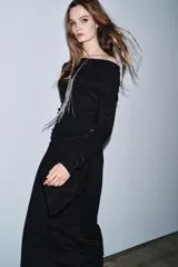 Vestido largo de color marrón oscuro, con cuello fluido tipo bote, manga larga y detalle de fruncido lateral con broche metálico en la cintura.