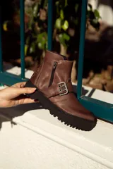Bota corta color marrón de cuero, con hebilla metálica y cierre lateral.