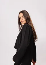 Camisa negra de cuello redondo con frunces y mangas largas con puños abiertos.