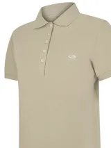 Chomba de piqué color beige con mangas cortas, cuello camisero y cierre frontal con cinco botones. Presenta un pequeño bordado del logo de la marca en el pecho.