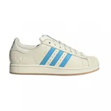 Championes Adidas Superstar edición especial Messi, color crema con las icónicas tres tiras en azul celeste. Presenta el logo de Messi grabado en el lateral y en el talón, con la clásica puntera de goma y suela de color goma.