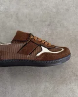 Championes de cuero vacuno con diseño de paneles en tonos marrones y detalles en blanco. Presentan una combinación de texturas lisas y grabadas, con cordones planos y costuras decorativas en la lengüeta.