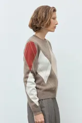 Sweater de punto con diseño de rombos en tonos tostado, beige y blanco, con detalles en color terracota en las mangas. Presenta cuello redondo y puños acanalados.