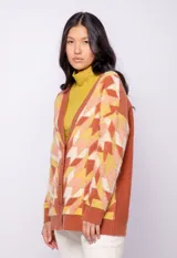 Cardigan de tejido de punto color ladrillo con diseño geométrico con relieve en tonos amarillo, naranja y blanco. Tiene escote en v y cierre con cinco botones de plástico.