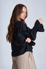 Blusa de color marrón con escote en V, mangas largas abullonadas con puños elásticos y detalles de volados en los hombros y el frente.