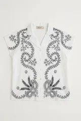 Camisa blanca de manga corta con cuello solapa, cierre frontal de botones y diseño bordado en hilo azul marino con motivos florales y vegetales.