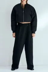 Pantalón sastrero negro de corte holgado, con diseño cruzado asimétrico en el frente, pinzas y piernas amplias.