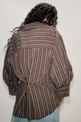 Camisa de cuello solapa con estampado de rayas verticales en tonos marrón y blanco. Presenta mangas abullonadas por debajo del codo con puños definidos y cierre frontal con botones.